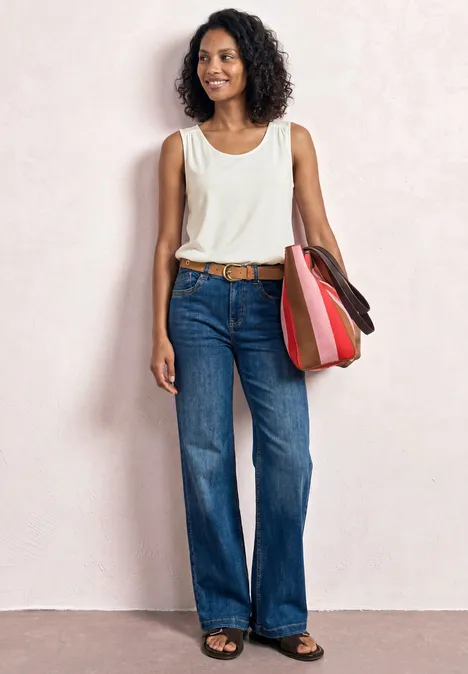 Top aus Jersey mit Elastiksaum off white Frau in weißem Ärmelloser Top, weitem Jeans und bunter Schultertasche vor hellem Hintergrund.