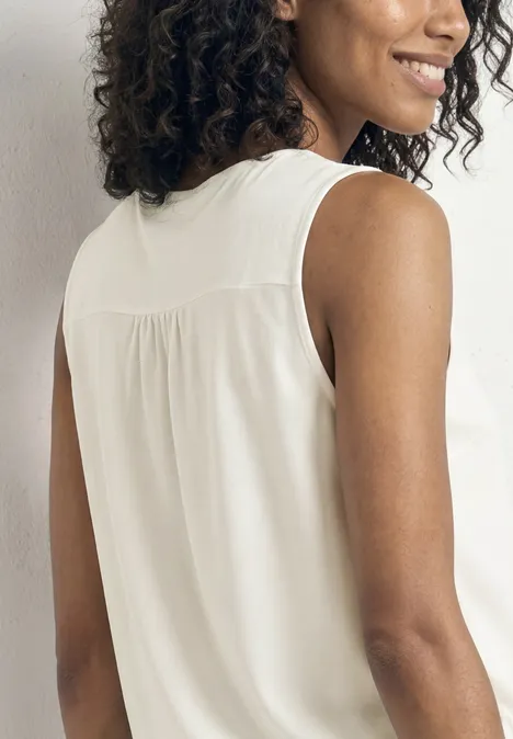 Top aus Jersey mit Elastiksaum off white Frau mit lockigem Haar im weißen ärmellosen Top, Blick über die Schulter vor neutralem Hintergrund