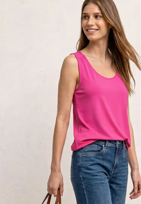 Eine Person trägt ein pinkes ärmelloses Oberteil und blaue Jeans, hält eine Tasche