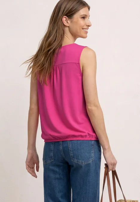 Frau von hinten in pinkem, ärmellosem Top, Jeans und brauner Tasche vor hellem Hintergrund.
