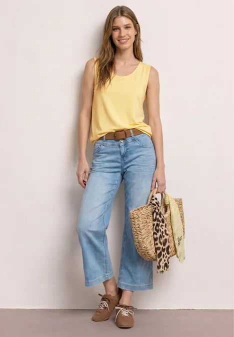 Frau mit gelbem Top, weitem Jeans-Culotte, braunem Gürtel und Korbtasche mit Leopardenmuster.