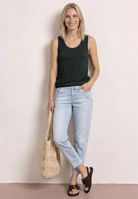 Frau im schwarzen Top, hellen Jeans und schwarzen Sandalen, trägt einen gehäkelten Strohbeutel.
