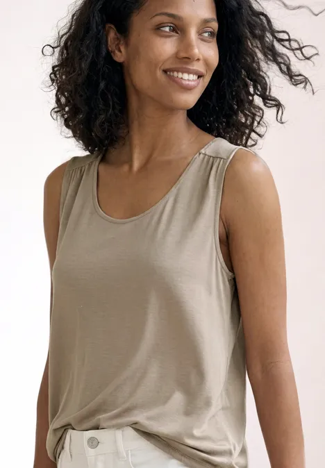 Top aus Jersey mit Elastiksaum sepia sand Frau mit lockigem Haar trägt beige ärmelloses Shirt vor hellem Hintergrund.