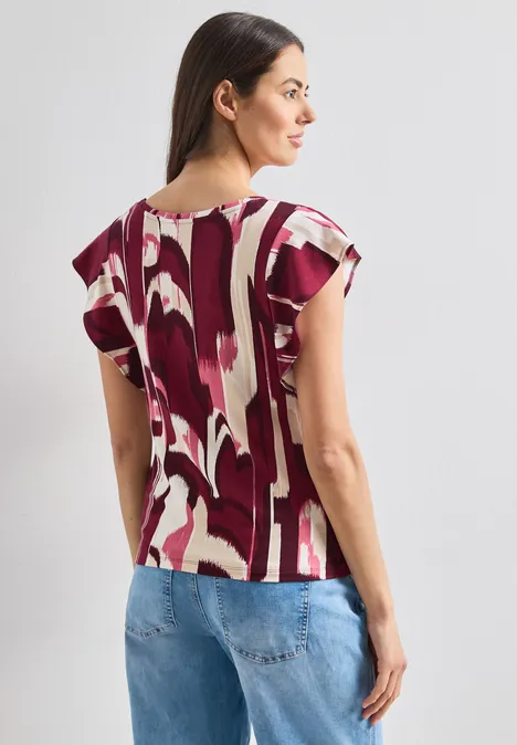 Vrouw van achteren in een rood-wit patroon top en een blauwe jeans.