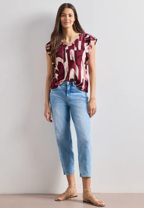 Een vrouw draagt een T-shirt met korte mouwen en print, blauwe jeans en sandalen.