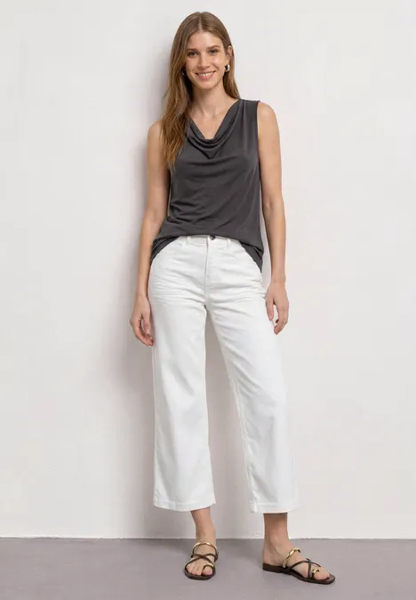Top aspect soyeux avec décolleté cascade espresso brown Femme en top sans manches gris foncé, pantalon blanc ample et sandales devant un fond sobre.