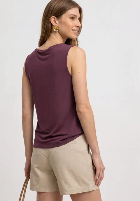 Vrouw van achteren in paars mouwloos topje en beige short, met een tas in haar hand.