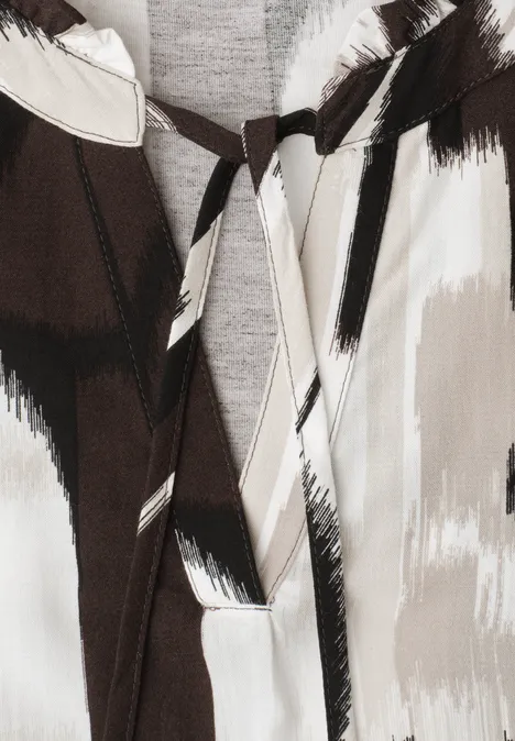 Detailaufnahme eines Kleidungsstücks mit abstraktem Pinselstrich-Muster in Schwarz, Beige und Weiß, mit Schluppe am Ausschnitt