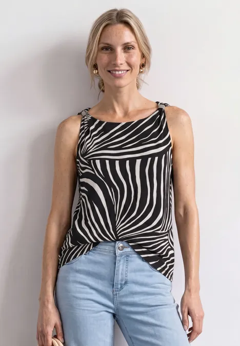 Vrouw voor een witte muur, met een zwart-wit gestreept topje en lichtblauwe jeans.
