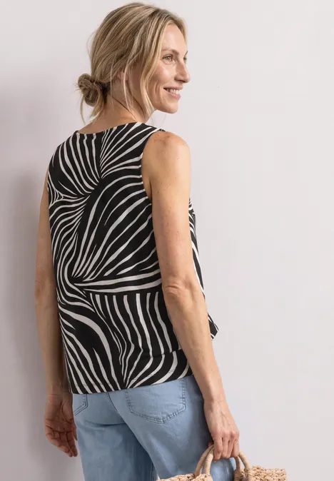 Vrouw van achteren in zebra-print top, blond knotje, spijkerbroek en strooien tas