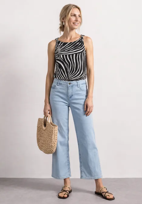 Vrouw met zebraprint top, lichte wijde jeans, zwarte sandalen en een strotas.