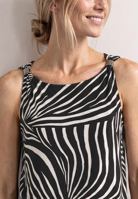 Vrouw die glimlacht draagt een mouwloze top met zebraprint en heeft haar opgestoken.