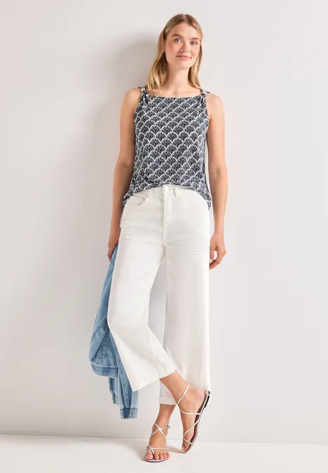 Femme en top à motifs, pantalon culotte blanc et sandales, décontractée avec une veste bleu clair.