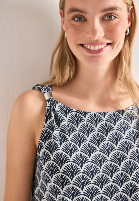 Une jeune femme porte un haut sans manches noir et blanc à motif feuillage devant un fond beige.
