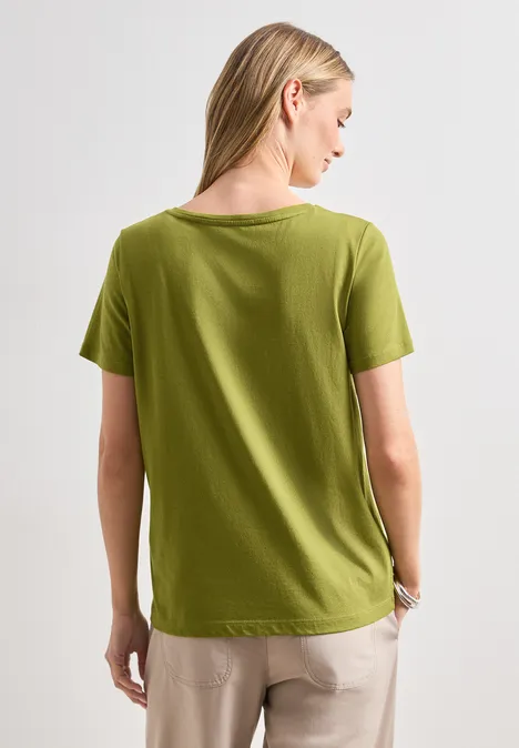 Rückansicht einer Frau in grünem T-Shirt und beiger Hose.
