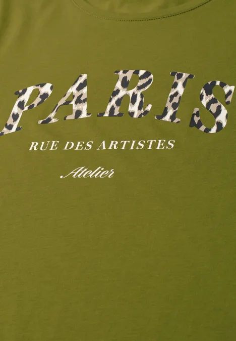 Ein olivgrünes T-Shirt mit dem Schriftzug 'PARIS' in Camouflage-Muster, darunter 'RUE DES ARTISTES' und 'Atelier' in Weiß.