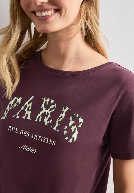 Frau trägt Burgunderfarbenes T-Shirt mit Blumen-Print 'PARIS' und Schriftzug 'Rue des Artistes'.