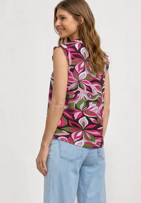 Frau von hinten in buntem, ärmellosem Top mit pink-grünem Blumenmuster und hellblauen, weiten Jeans.