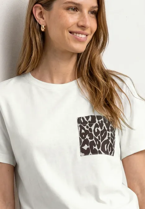 Frau trägt weißes T-Shirt mit schwarzem Leo-Muster auf der Brusttasche.
