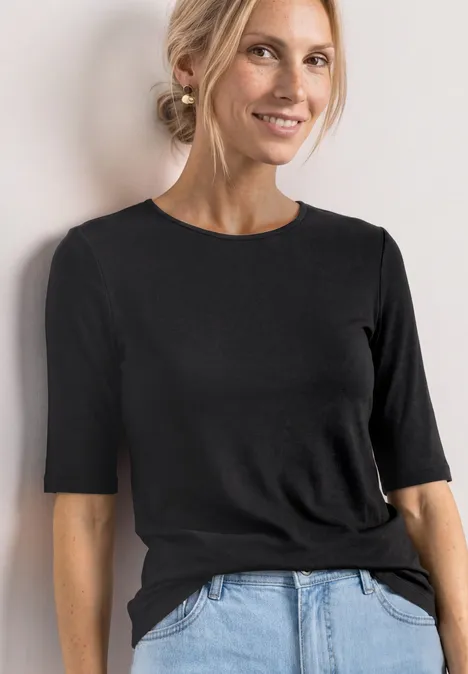Frau ohne erkennbare Gesichtszüge trägt eng anliegendes schwarzes Shirt mit 3/4-Ärmeln und blaue Jeans.