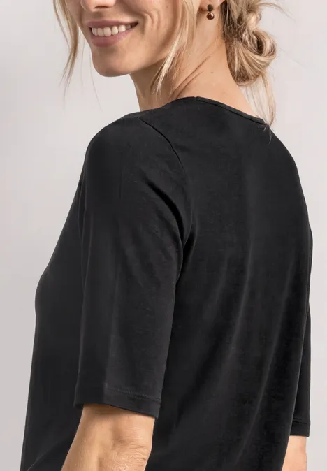 Frau im schwarzen Halbarmshirt, von hinten fotografiert, mit lockerem Dutt und dezentem Ohrschmuck.