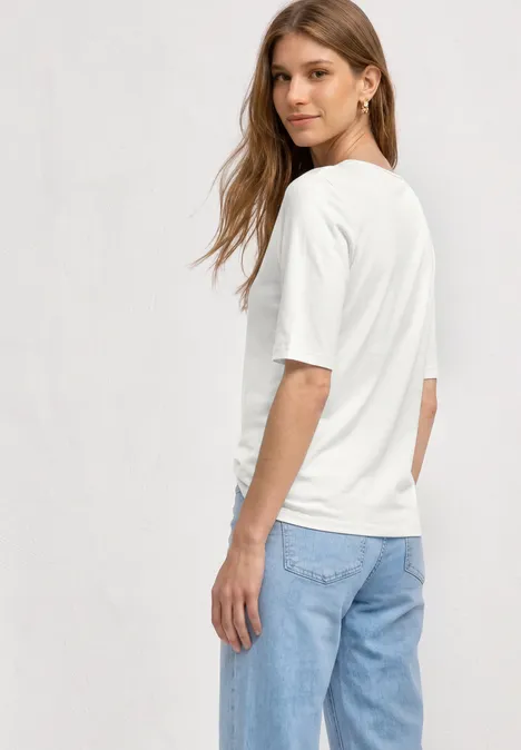 Frau von hinten in weißem T-Shirt und blauen Jeans vor hellem Hintergrund.