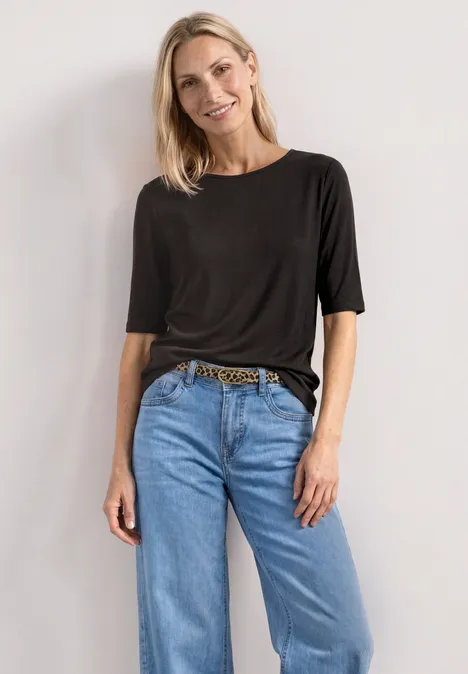 Frau in schwarzem T-Shirt, hellblauen Jeans und Leoparden-Gürtel vor weißem Hintergrund.
