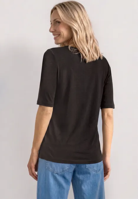 Person von hinten in schwarzem T-Shirt, blonden schulterlangen Haaren und blauen Jeans.