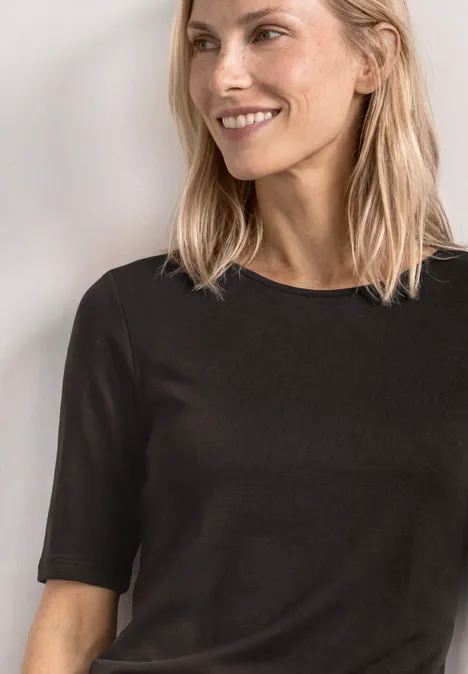 Frau mit blonden Haaren trägt ein schlichtes schwarzes T-Shirt mit kurzen Ärmeln.