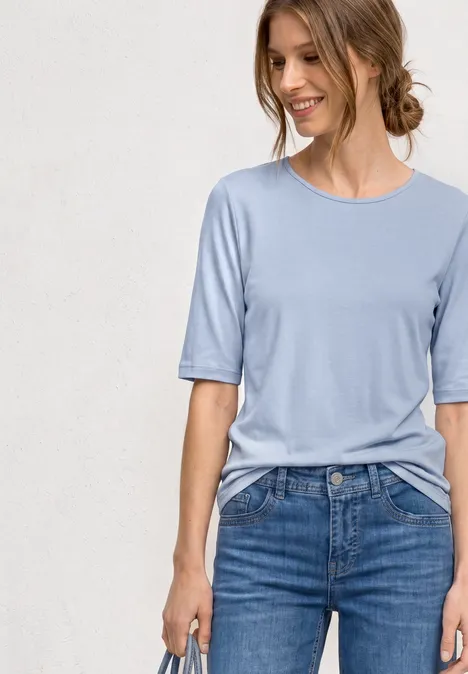 Frau trägt hellblaues T-Shirt mit halb langen Ärmeln und blaue Jeans.