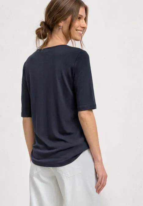 Dame von hinten in locker sitzendem dunkelblauem T-Shirt mit Halbarm und hellen Hosen.