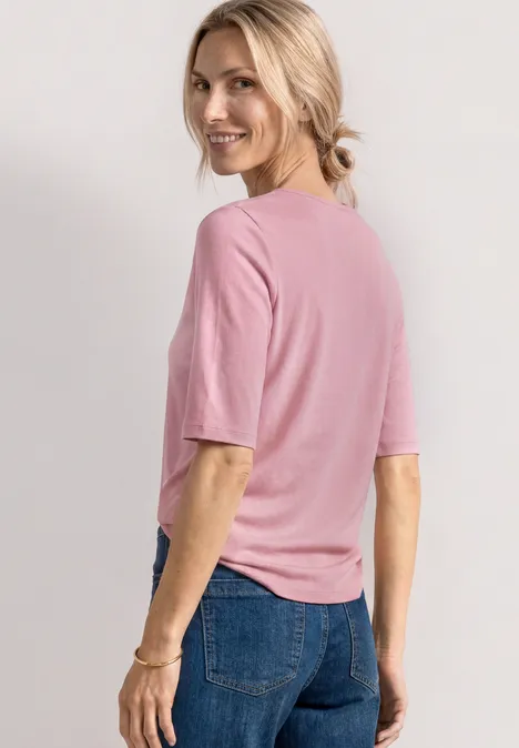 Rückansicht einer Person mit rosa Halbarmshirt und blauer Jeans, blonde Haare im Pferdeschwanz.