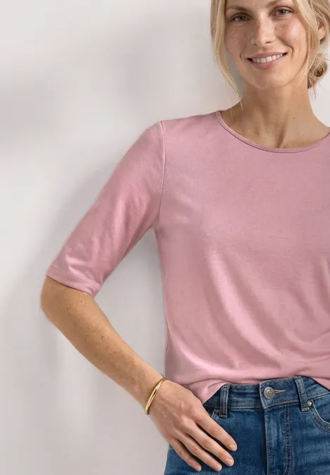 Frau in rosa Kurzarmshirt, lässig in blaue Jeans gesteckt, minimalistischer Casual-Look.