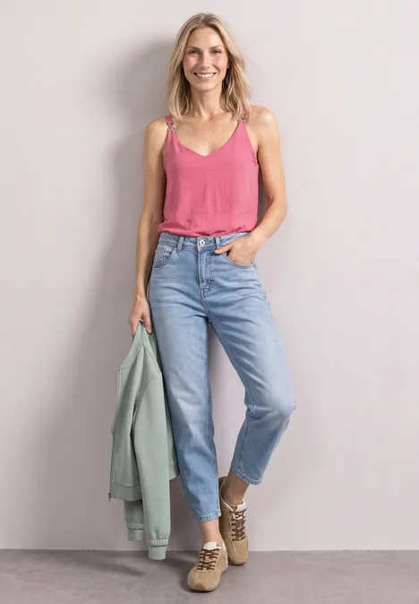 Top mit V-Neck und Dekodetail blush berry Eine lächelnde Frau in pinkem Top, Jeans, beigen Stiefeletten und grüner Jacke vor grauem Hintergrund.