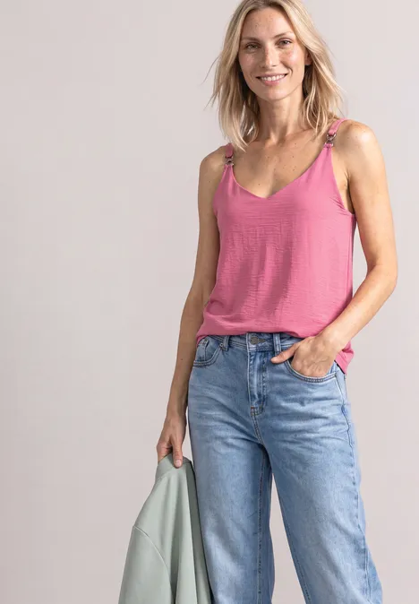 Top mit V-Neck und Dekodetail blush berry Eine lächelnde Frau in rosa Top und Jeans, hält eine hellgrüne Jacke in der Hand.