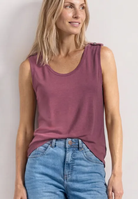 Femme en top rose sans manches et jean bleu devant un fond clair.