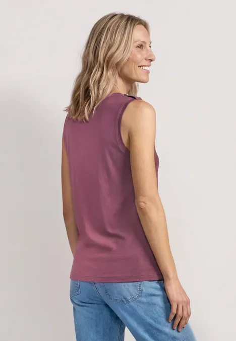 Vue de dos d'une femme aux cheveux blonds portant un débardeur violet et un jean bleu.