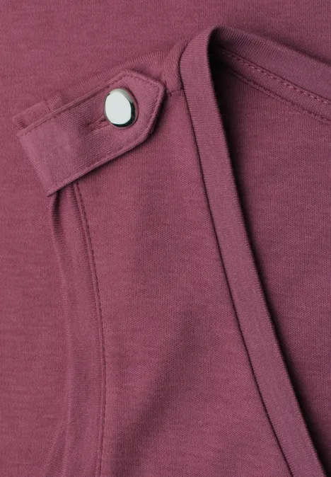 Gros plan d’un t-shirt bordeaux avec un petit passant et un bouton-pression argenté au col.
