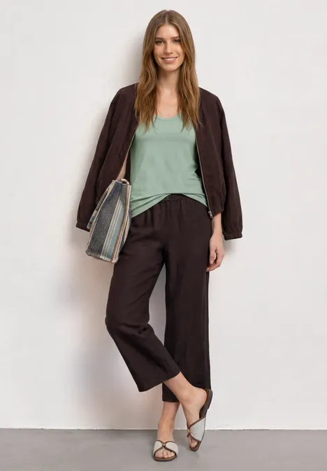 Top mit V-Neck und Knopfdetail eucalyptus green Eine Frau steht vor weißer Wand, trägt braunes Jacket, weite Hosen, mintgrünes Top, weiße Riemchensandalen und eine gestreifte Tasche.