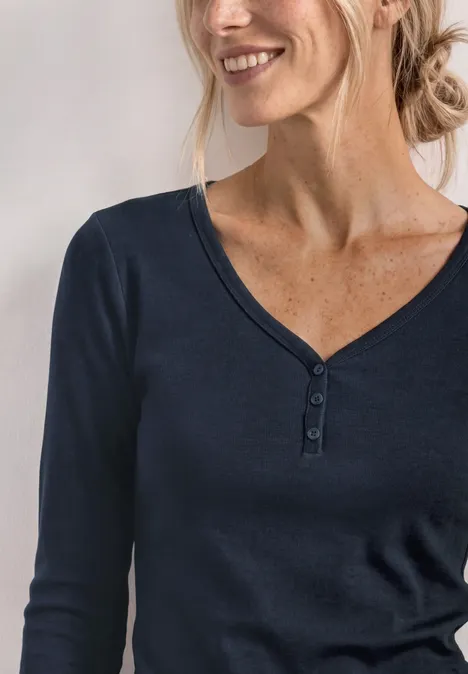 Eine lächelnde Frau in marineblauem Langarmshirt mit V-Ausschnitt und Knopfleiste.