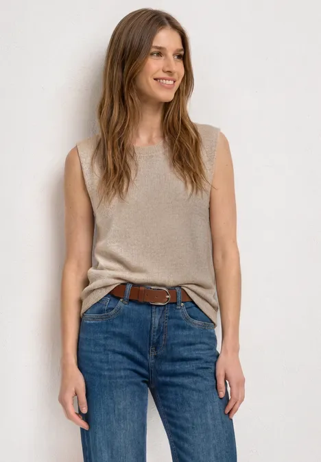 Top mit Rundhals und Glitzer clay sand Frau in ärmellosem beigem Top mit Knoten und blauen Jeans vor hellem Hintergrund.