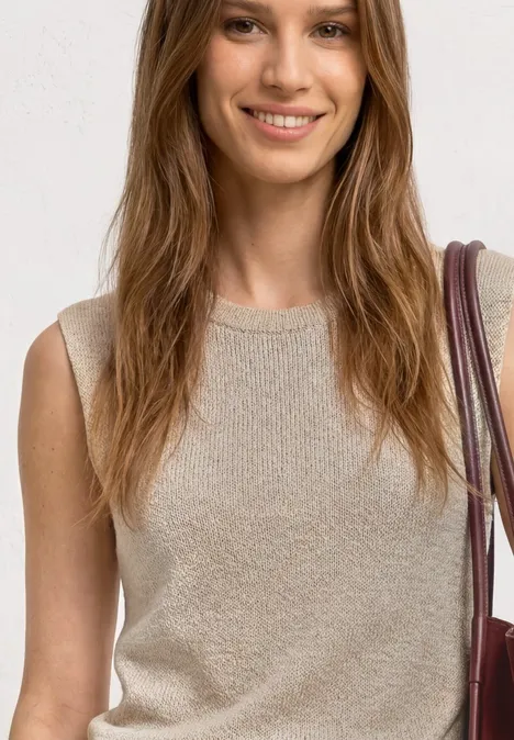 Top mit Rundhals und Glitzer clay sand Lächelnde Frau im ärmellosen, beigen Stricktop mit Schultertasche, von der Taille aufwärts fotografiert.