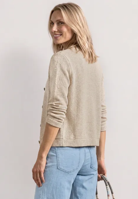 Frau von hinten in beigem Strickjäckchen und blauen Jeans, die eine Handtasche hält.