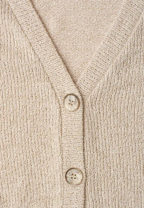 Nahaufnahme eines beigen, grob gestrickten Cardigans mit V-Ausschnitt und zwei Knöpfen.