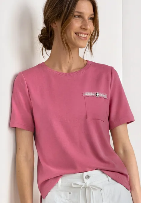 T-shirt avec poche poitrine décorative blush berry Femme en tee-shirt rose avec poche poitrine et pantalon blanc devant un fond clair.