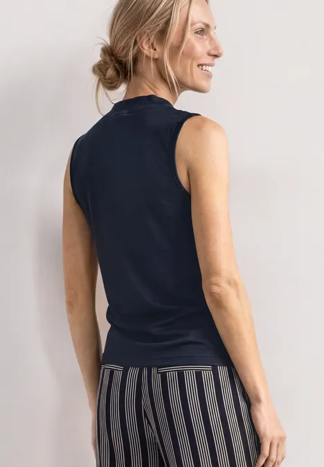 Silk-Look Top z golfem darkest blue Kobieta widziana od tyłu w czarnej bluzce bez rękawów i w pasiastych spodniach.