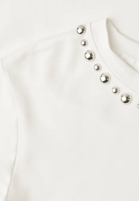 Haut blanc orné de rivets métalliques argentés autour de l'encolure.