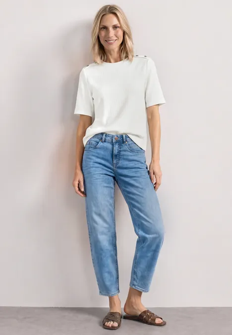 T-shirt à col rond avec boutons off white Femme en t-shirt blanc, jean bleu décontracté et sandales marron devant un fond neutre.