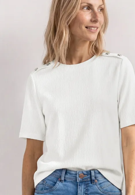T-shirt à col rond avec boutons off white Femme en t-shirt blanc à manches courtes avec boutons aux épaules et jean bleu, torse visible, visage flou.