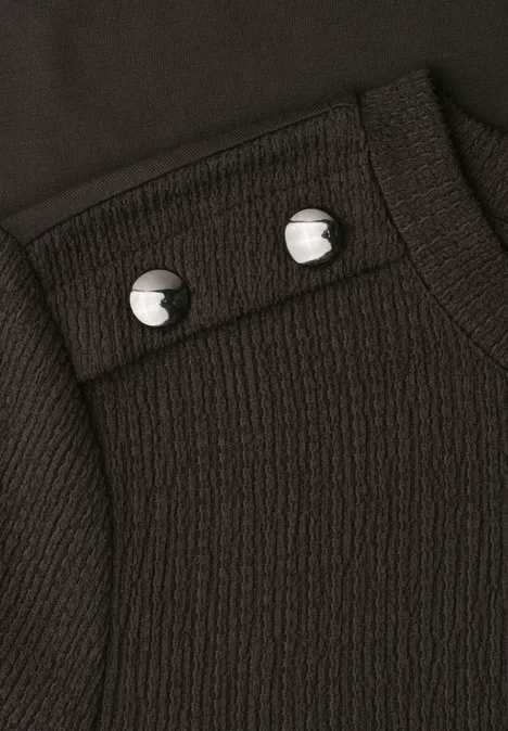 Nahaufnahme eines schwarz strukturierten Kleidungsstücks mit zwei silbernen Druckknöpfen.